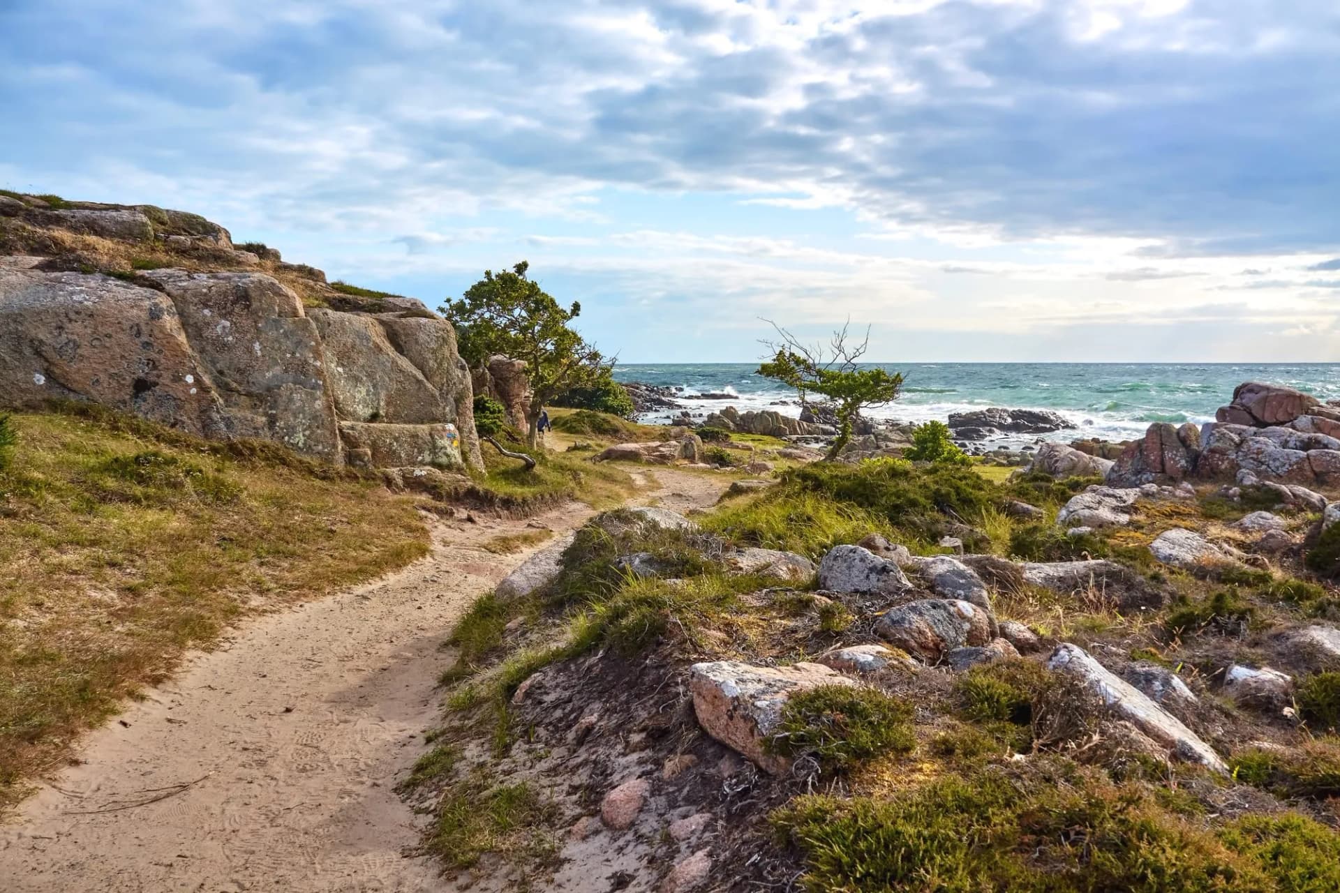 Hiking path along rocky coastline toward Sandvig under cloudy sky