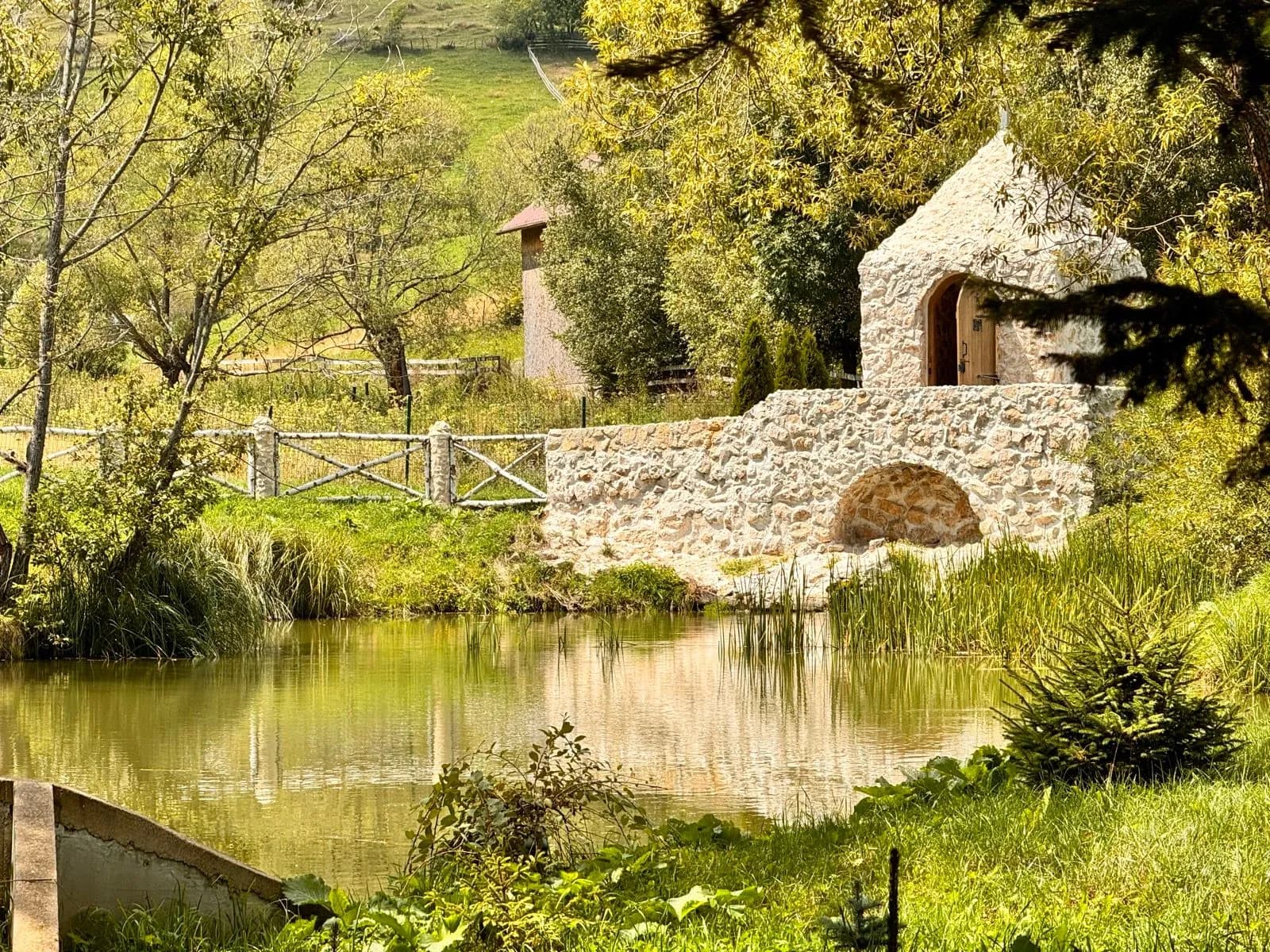 Stone structure with arched bridge over pond, surrounded by lush green landscape near Moeciu de Sus.