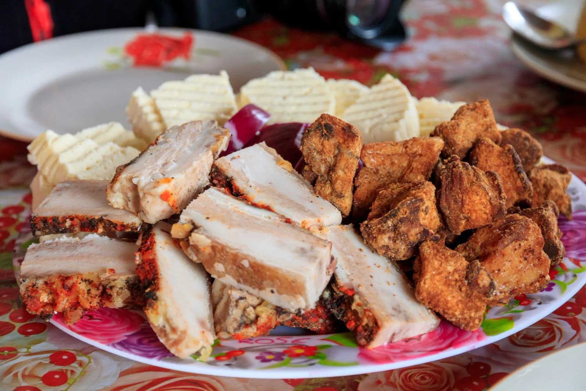 Platter of sliced cured pork belly, fried pork pieces, and butter with red onion slices, Romanian food.