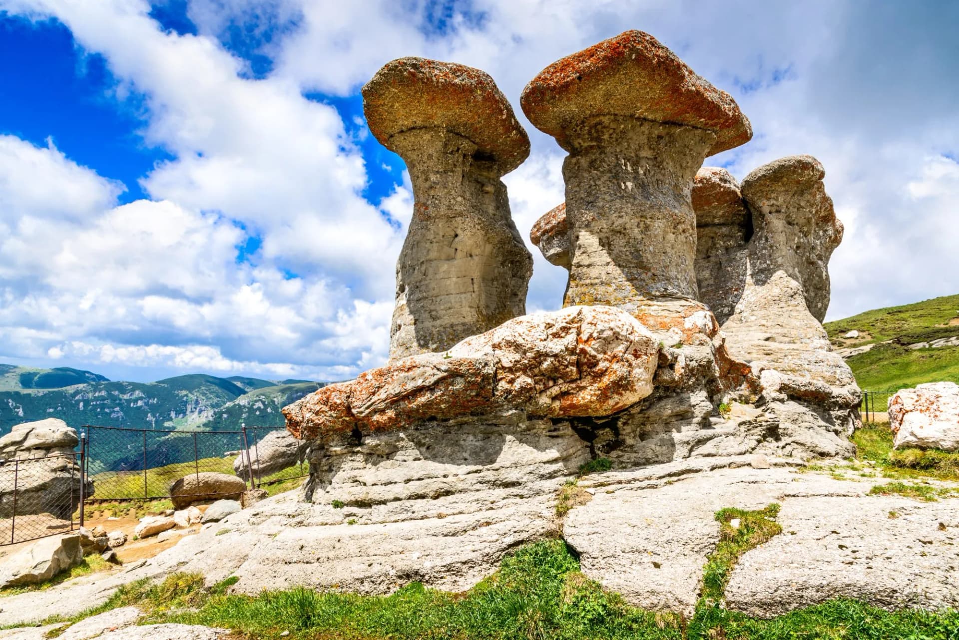 Mushroom-shaped rock formations under blue sky with white clouds in a mountainous landscape