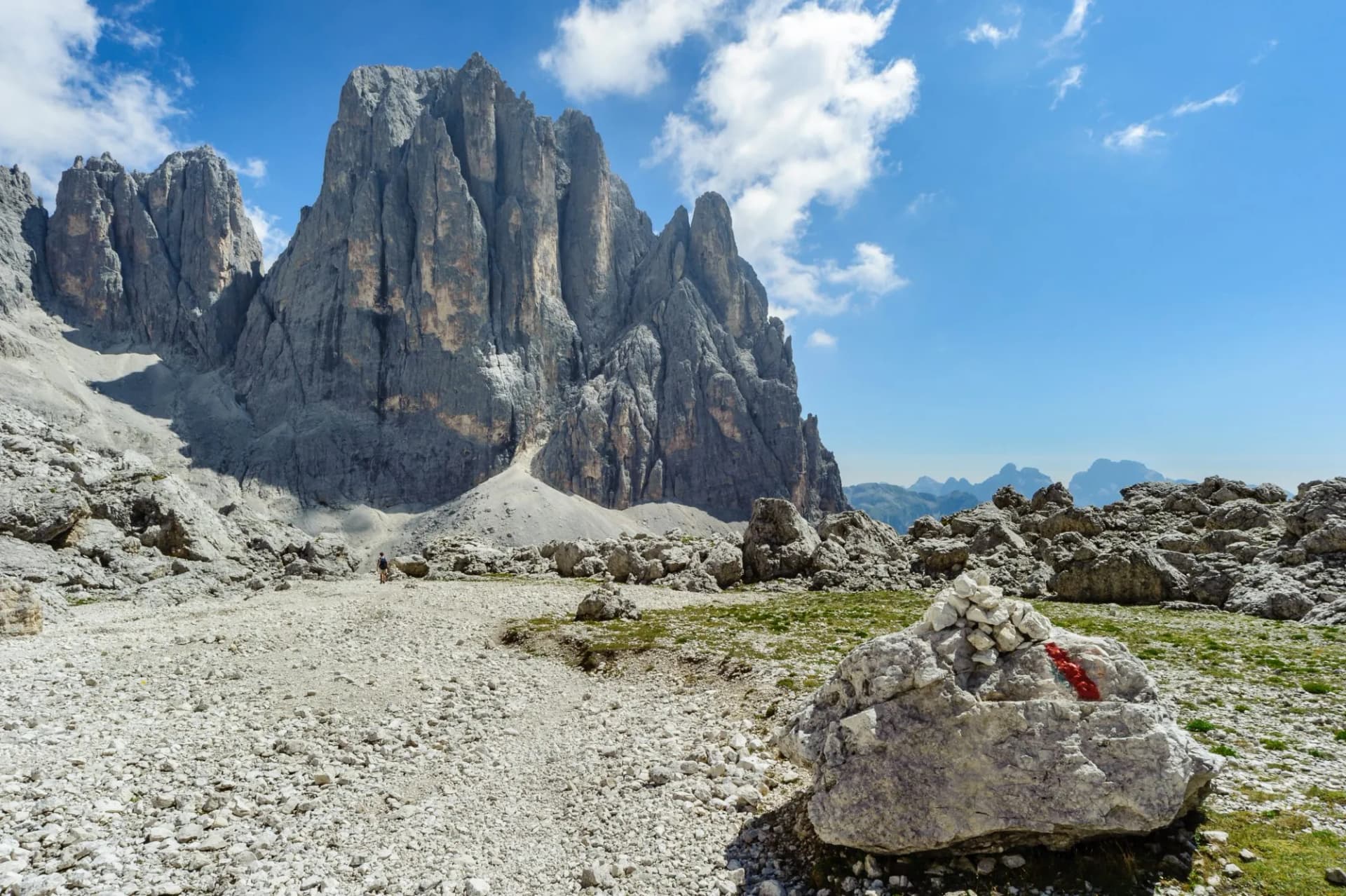 Hiking near massive rock towers of Pale di San Martino mountains under blue sky.