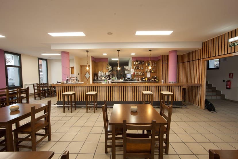 Bar area with wooden counter, stools, and dining tables in a brightly lit interior.
