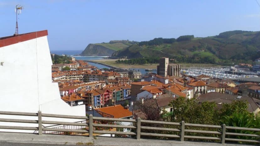 Coastal town with terracotta roofs, marina, and green hills, likely Albergue Convento de San José.