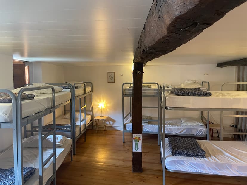 Dormitory room with metal bunk beds, wooden floors, and a large wooden support beam.
