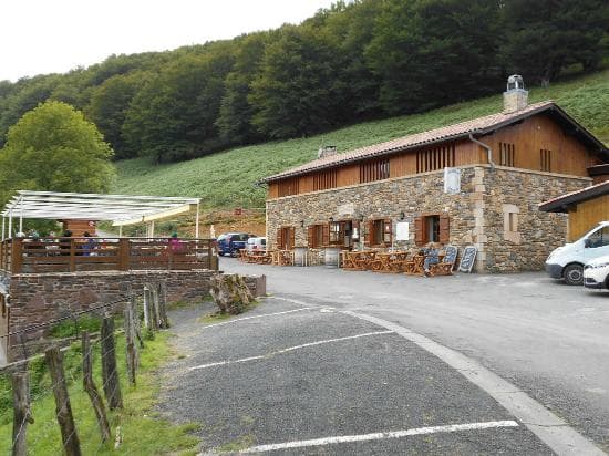 Stone refuge building with outdoor seating beside a steep, forested hillside, Refuge Orisson.