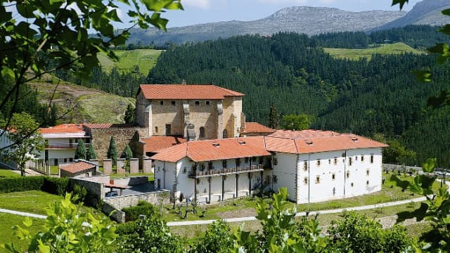 Monasterio de Zenarruza complex with white walls and orange tile roofs set against forested mountains.