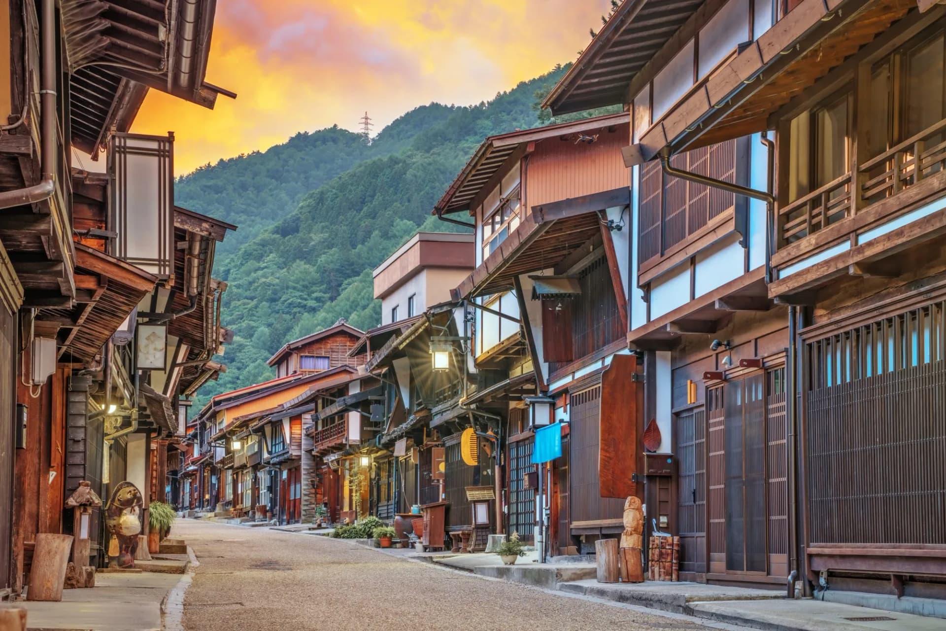 Historic street in Narai-juku with traditional wooden buildings and lush green mountains at sunset.