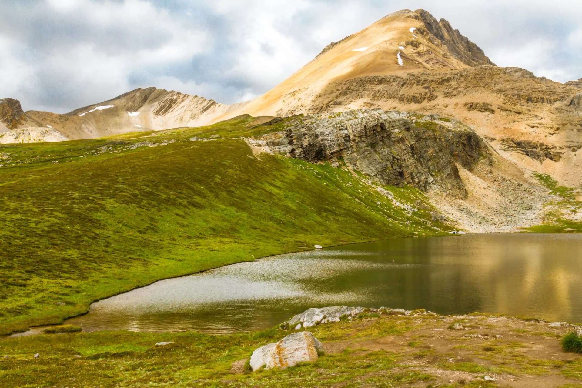 Alpine lake reflecting golden mountain under cloudy sky with green slopes