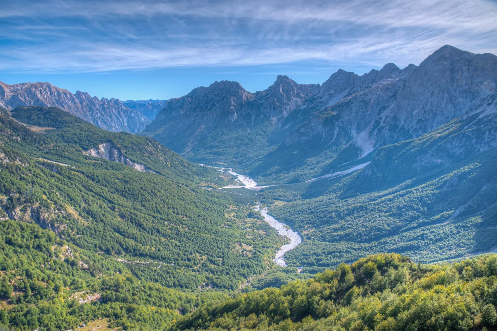Aerial view of Valbona Valley in Albania with a winding river and steep, forested mountains.