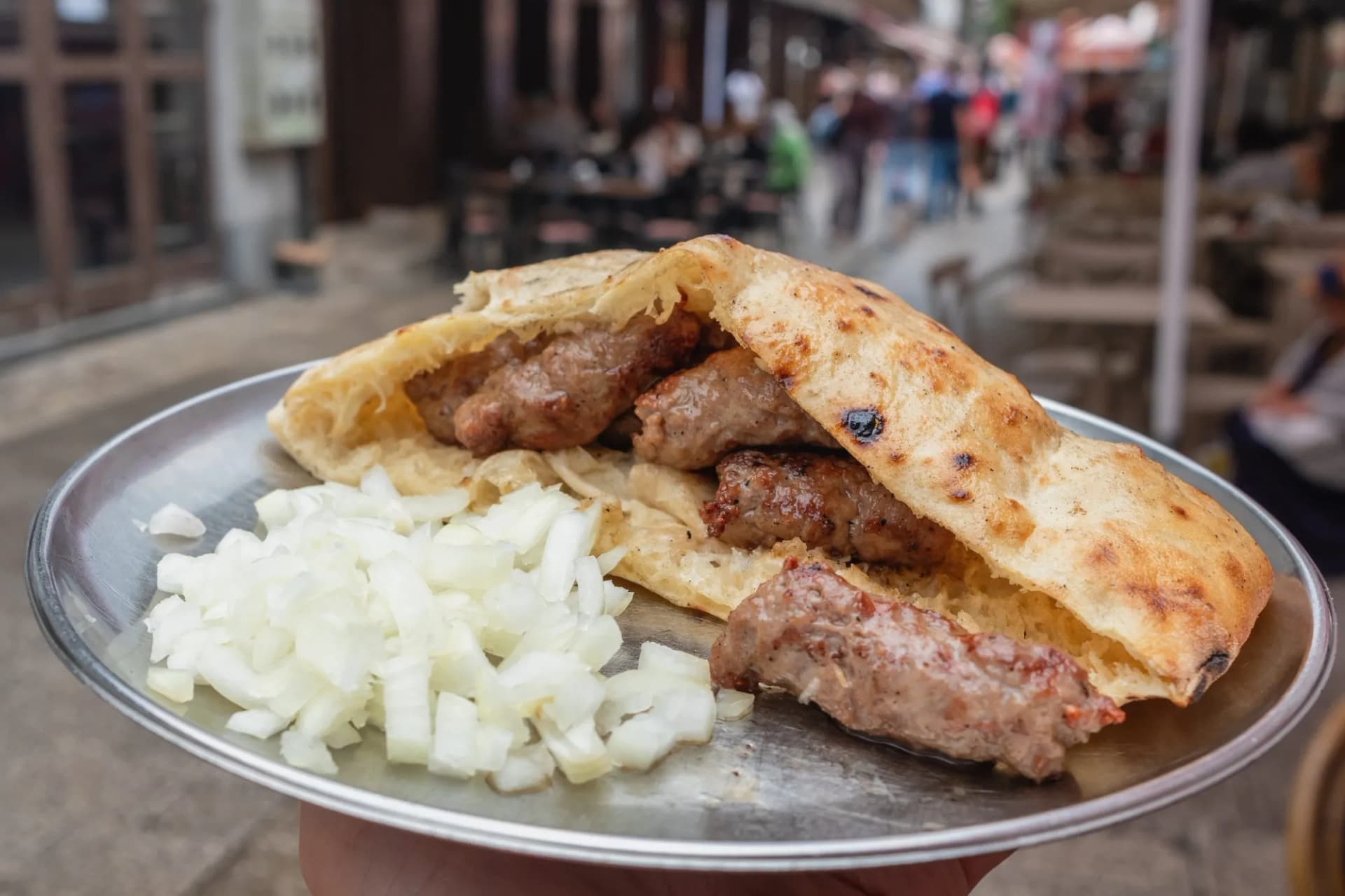 Traditional Bosnian ćevapi with chopped onions served on a metal plate in Sarajevo.