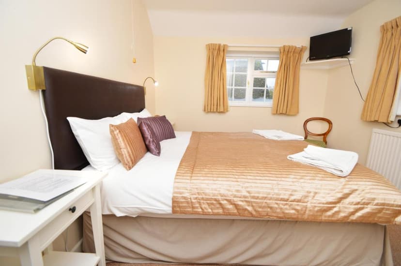 Cozy inn bedroom with double bed, white linens, brown headboard, and window view.