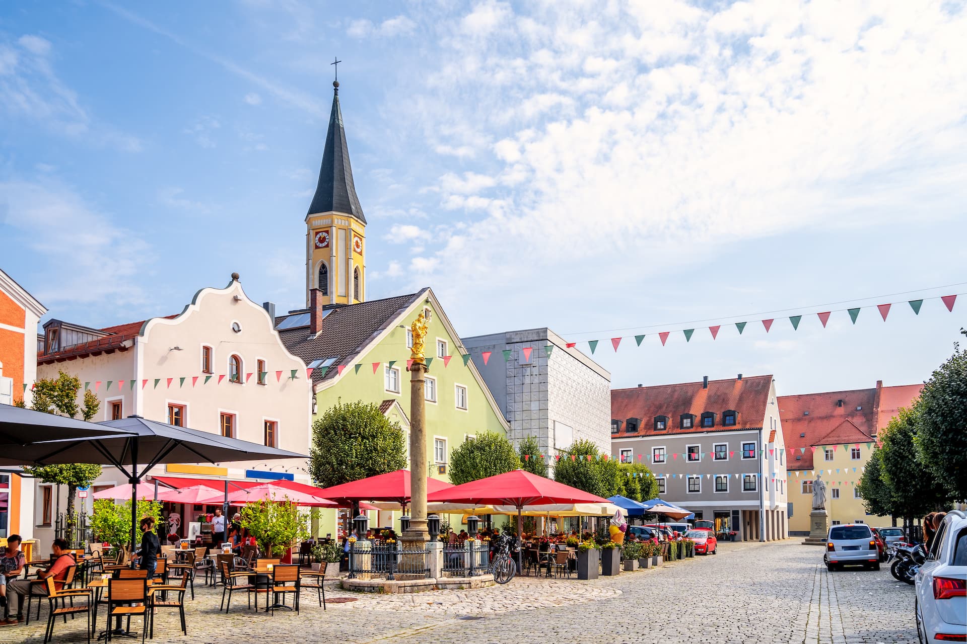 Outdoor cafe dining in Kelheim town square with church spire and colorful buildings.