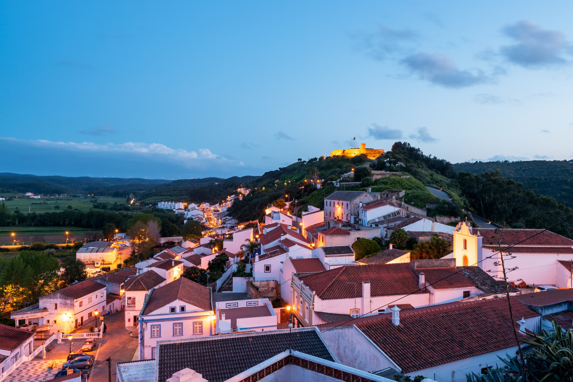 Night view of Aljezur town in Algarve, Portugal, with illuminated white buildings and castle on hill.