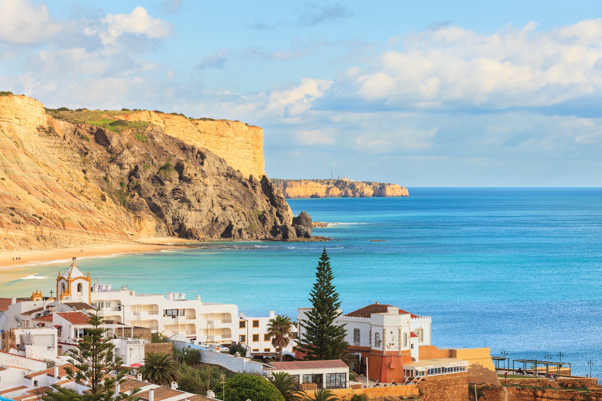 Coastal town with white buildings below orange cliffs overlooking turquoise sea at Praia da Luz, Lagos, Algarve, Portugal.