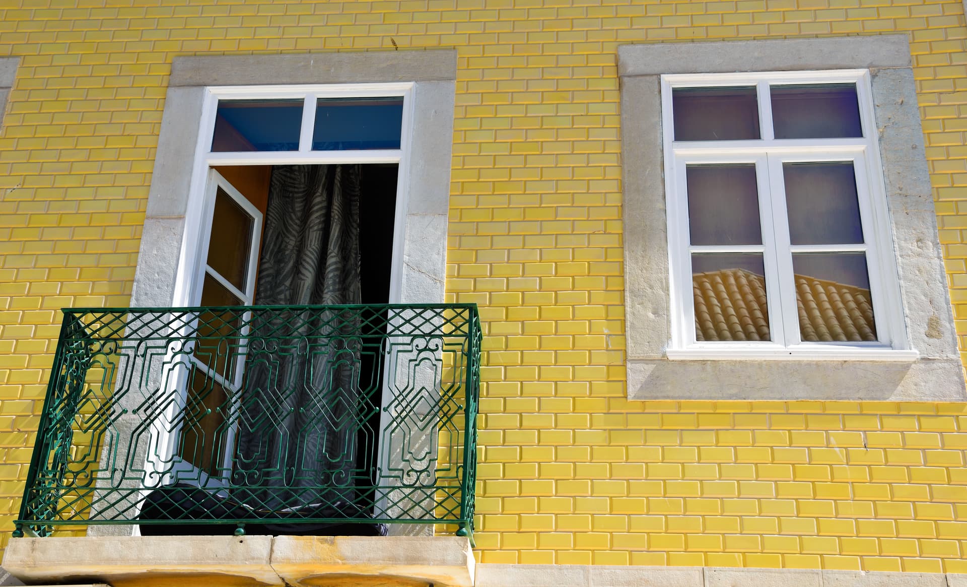 Yellow tiled building facade with green balcony railing and white window in Lagos, Algarve, Portugal.