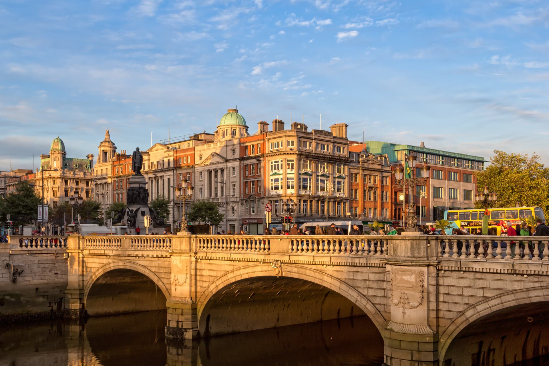 Stone bridge over river with historic buildings and statue at sunset in Dublin