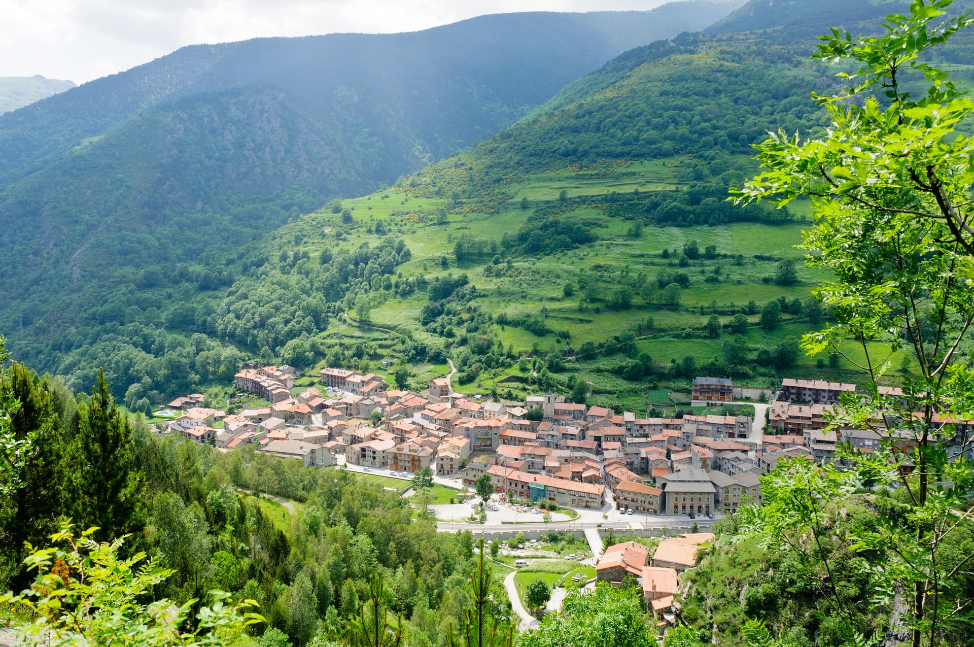 Village nestled in a green valley surrounded by forested mountains, view from above