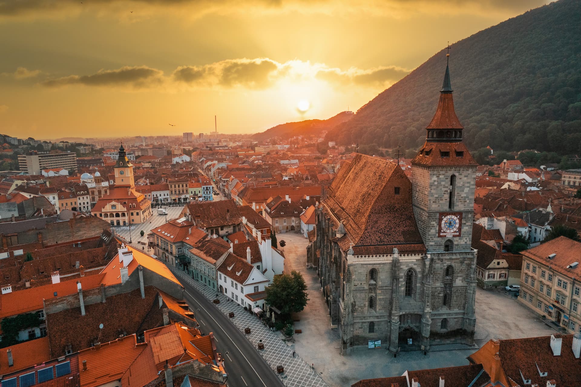 Black Church in Brasov overlooking city rooftops at sunset with a mountain backdrop.