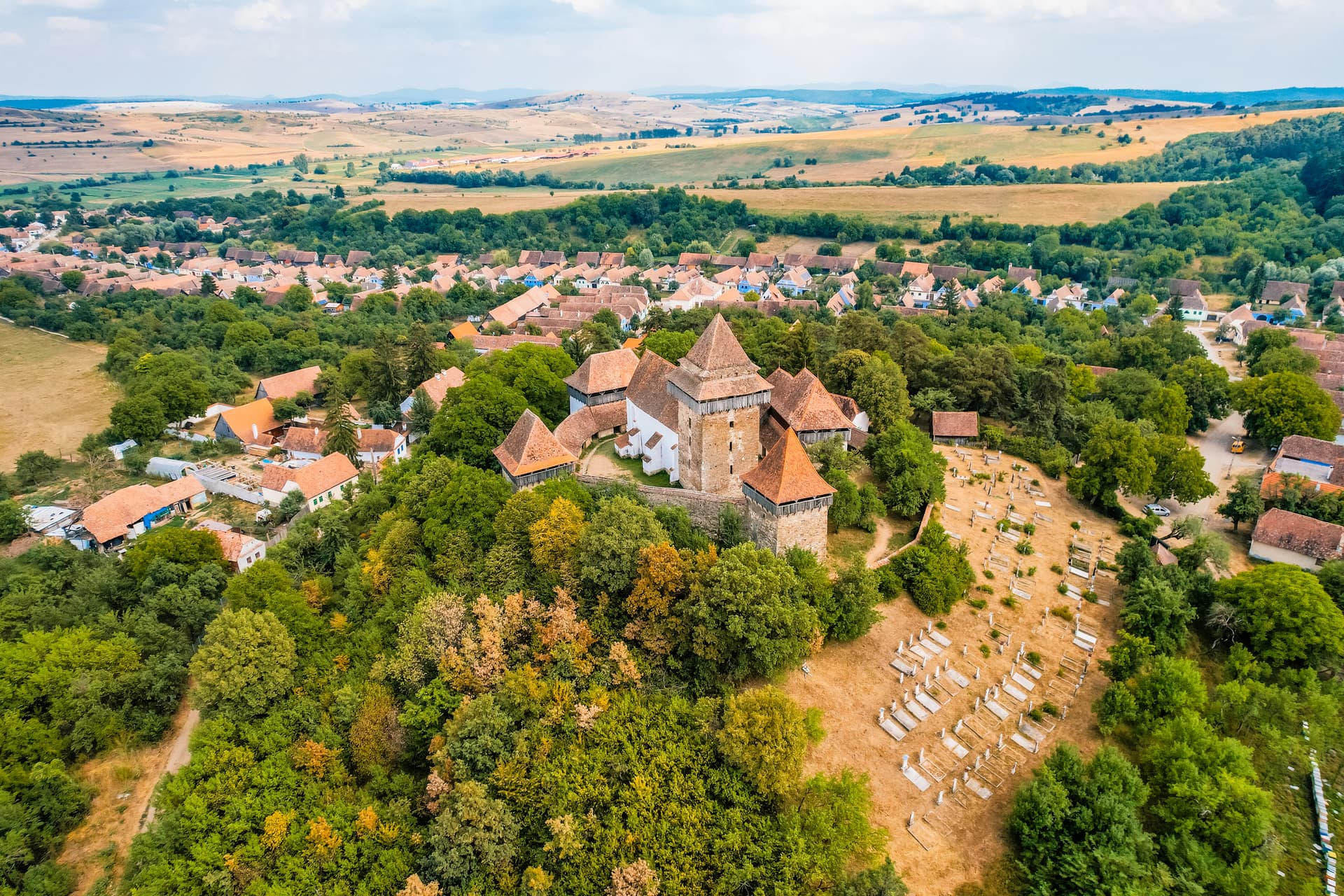 Aerial view of fortified church surrounded by village, trees, and rolling farmland.