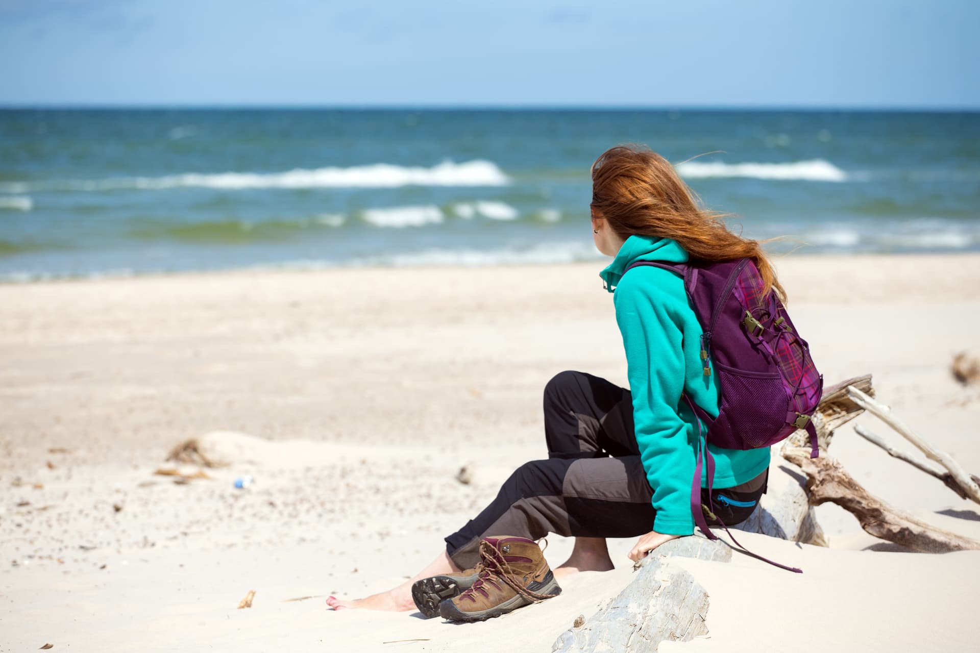 Hiker resting with backpack on sandy beach looking at ocean waves