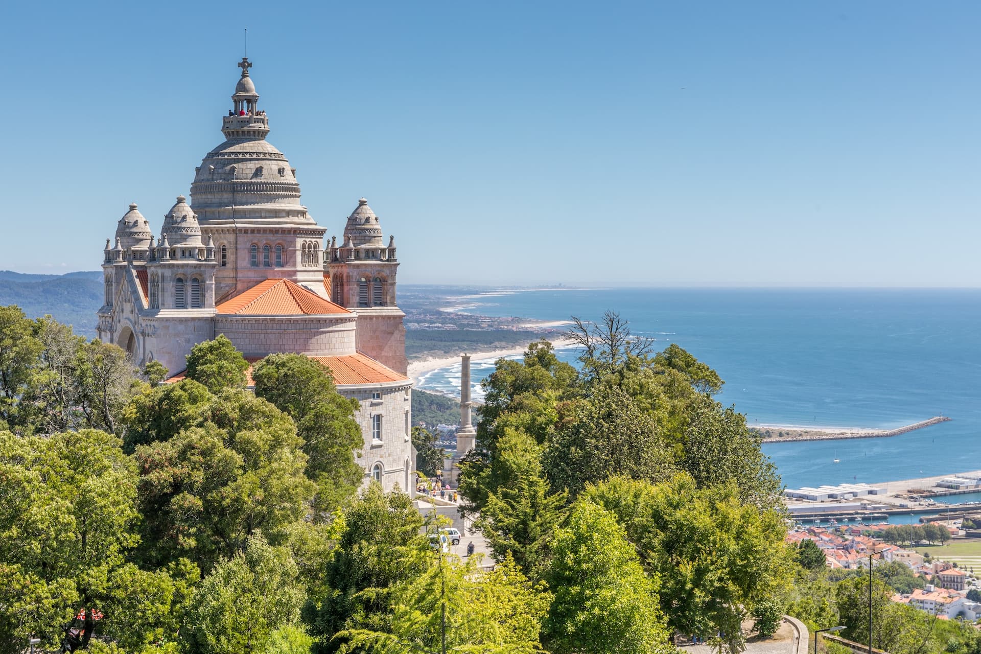 Santuário de Santa Luzia overlooking the coast and blue sea from a hilltop surrounded by green trees.