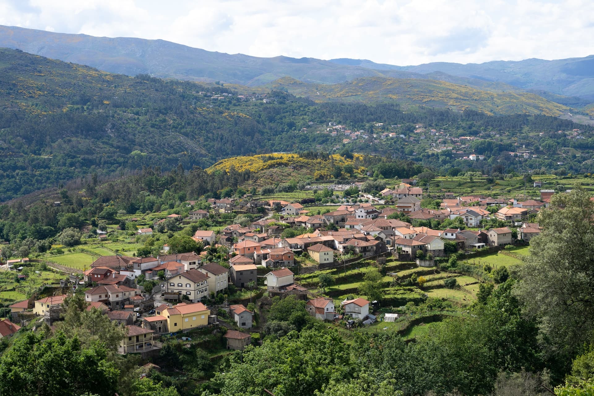 Village houses nestled in green terraces with forested mountains surrounding Soajo, Portugal.
