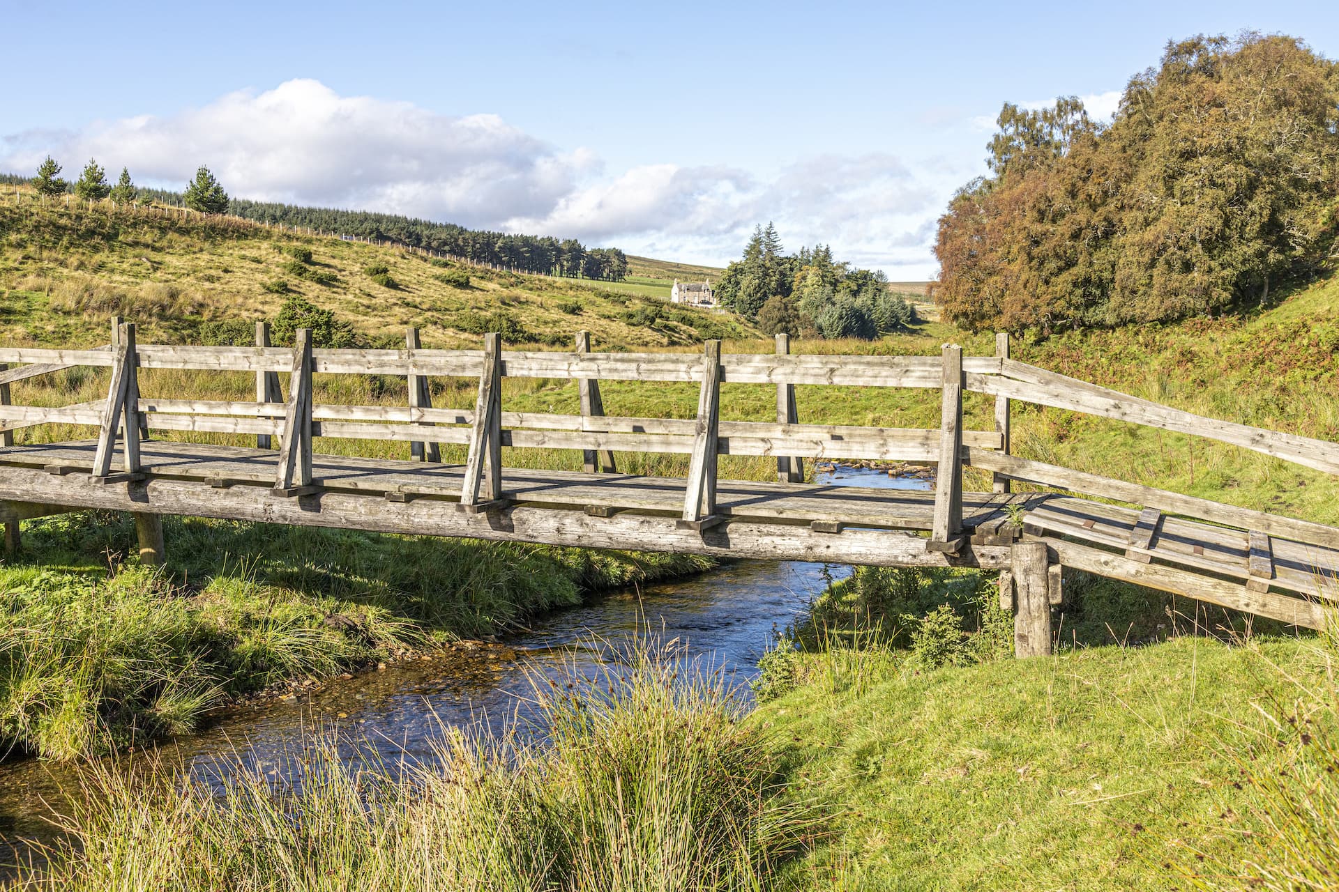 Wooden footbridge over a stream in grassy hills near Tomintoul, Scotland.