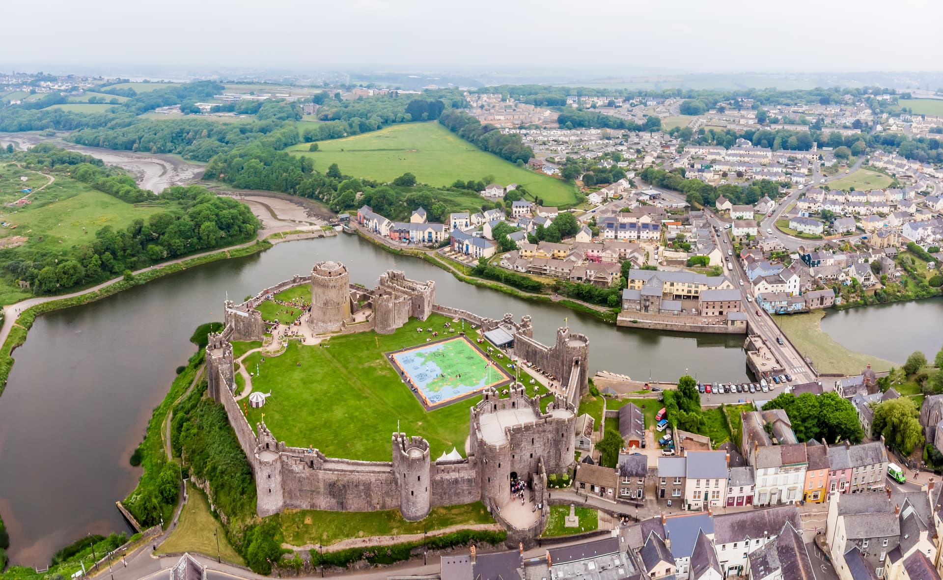 Aerial view of Pembroke Castle surrounded by a river and town buildings under an overcast sky.