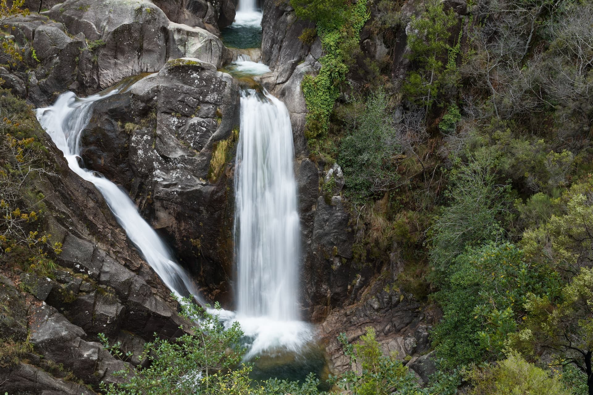 Waterfall cascading over dark rocks surrounded by lush green vegetation in Geres National Park, Portugal.