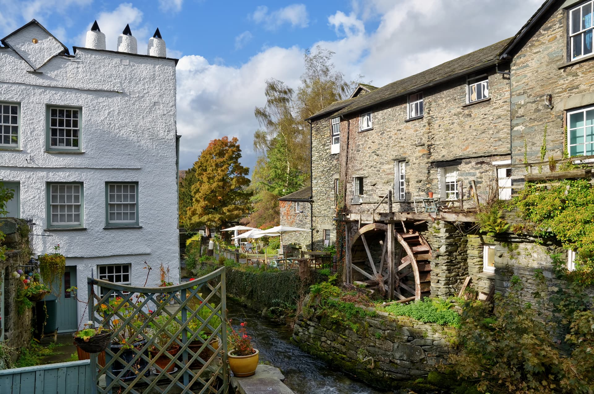 Waterwheel next to stone building and white cottage beside a stream in Ambleside.