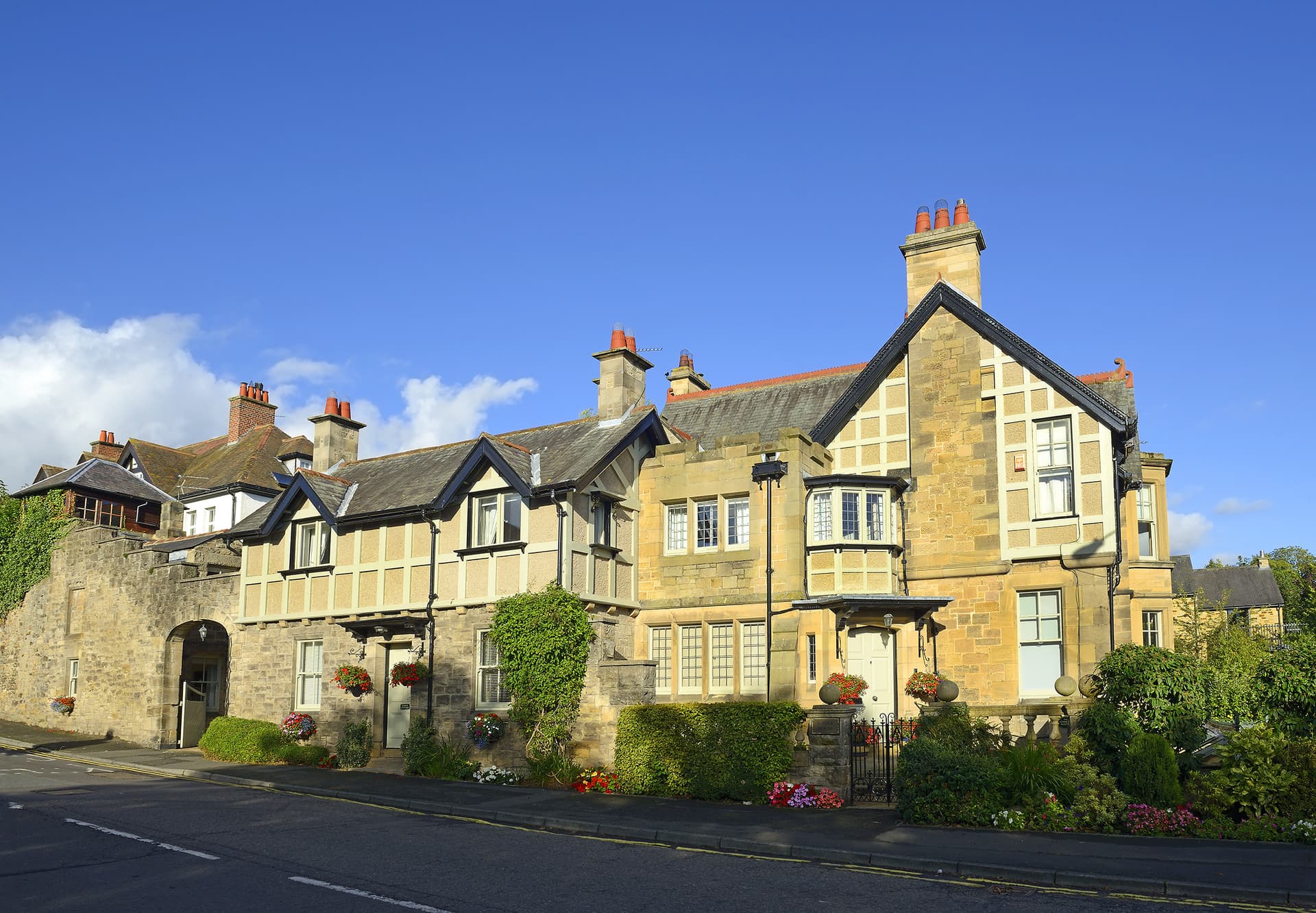 Stone and timber-framed houses with hanging flower baskets along a street under a blue sky in Corbridge.