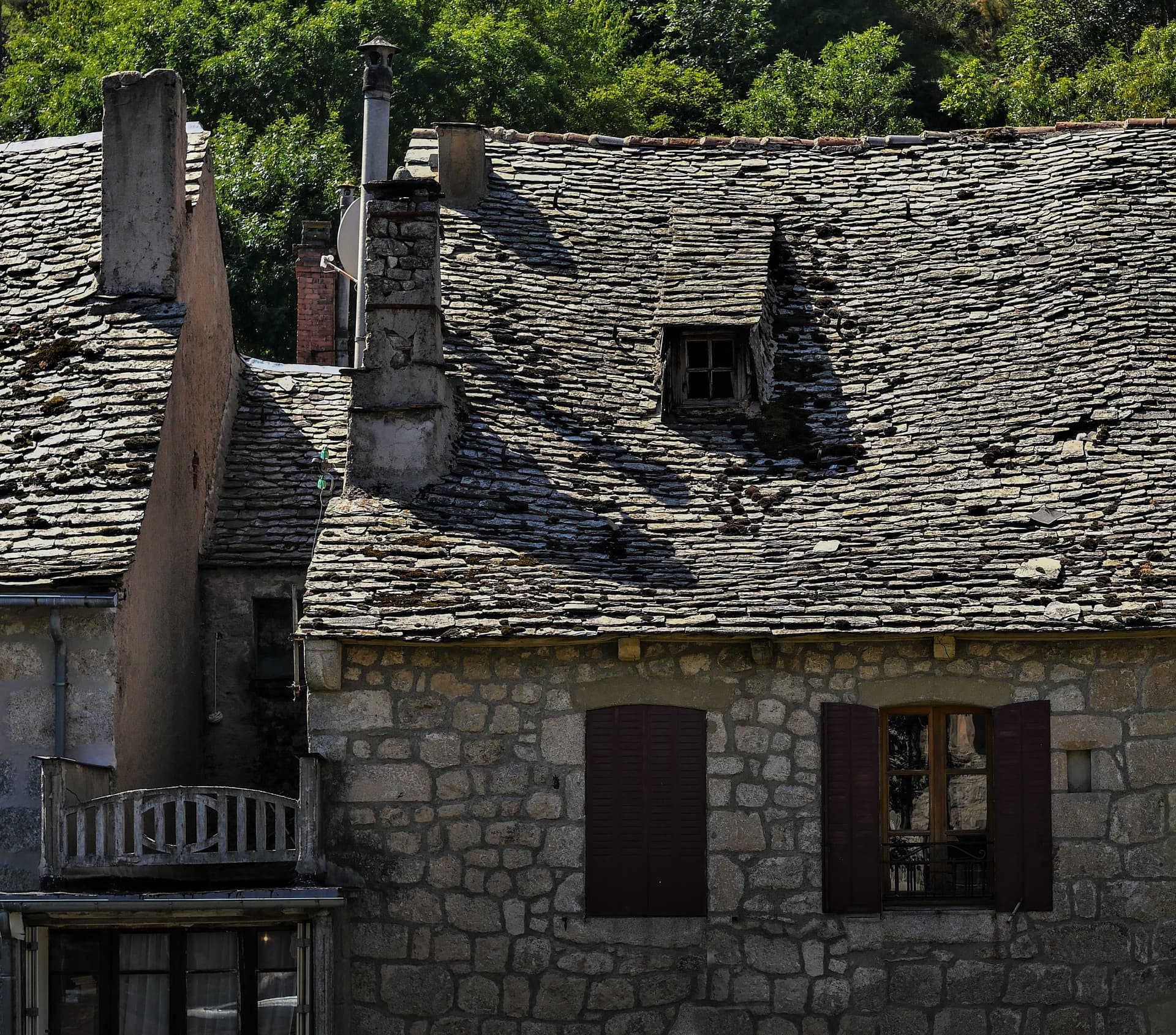 Stone buildings with slate roofs, chimneys, and dark wooden shutters in a French countryside village.