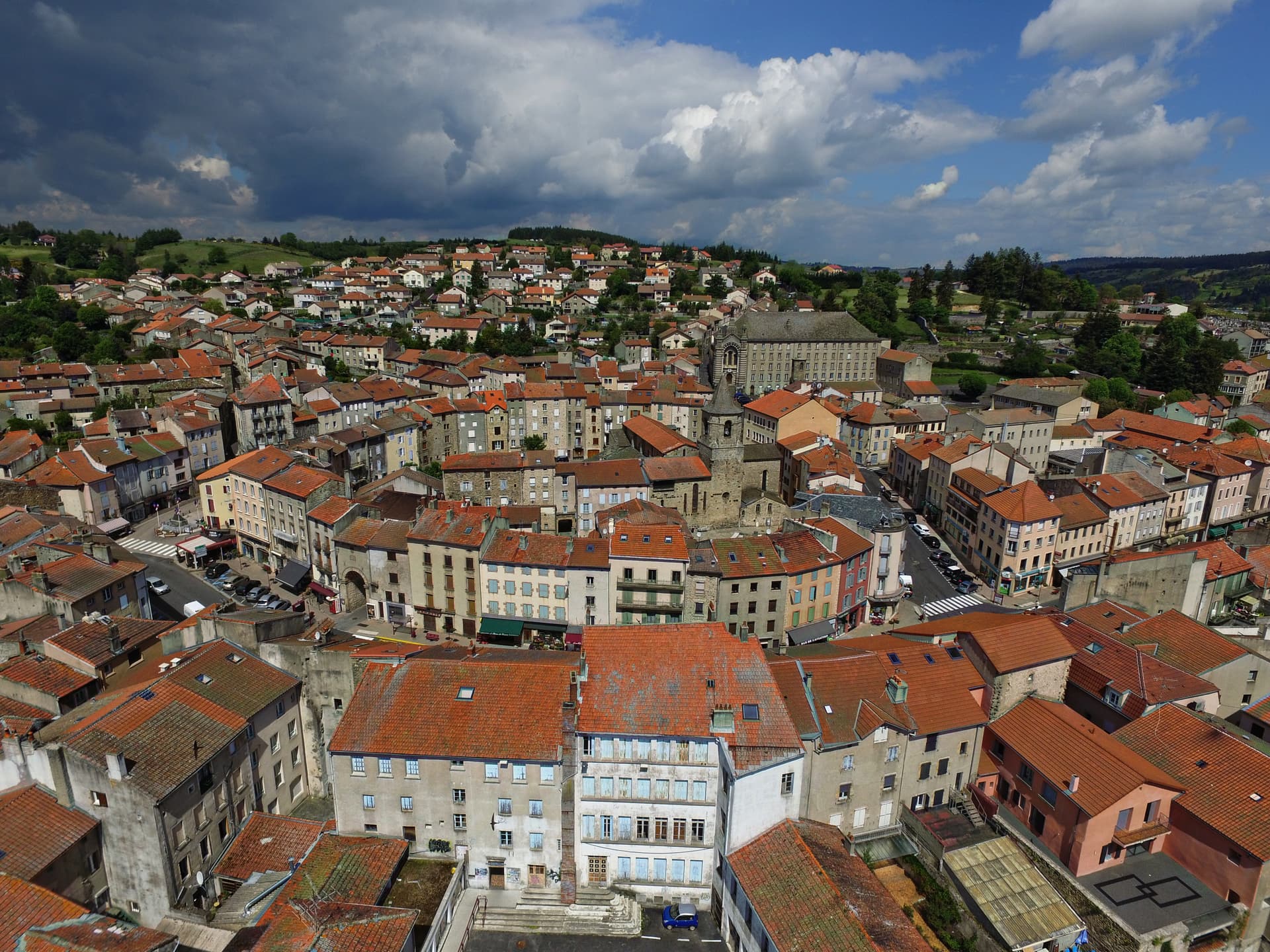 Aerial view of dense European town with terracotta roofs under dramatic blue and dark clouds.