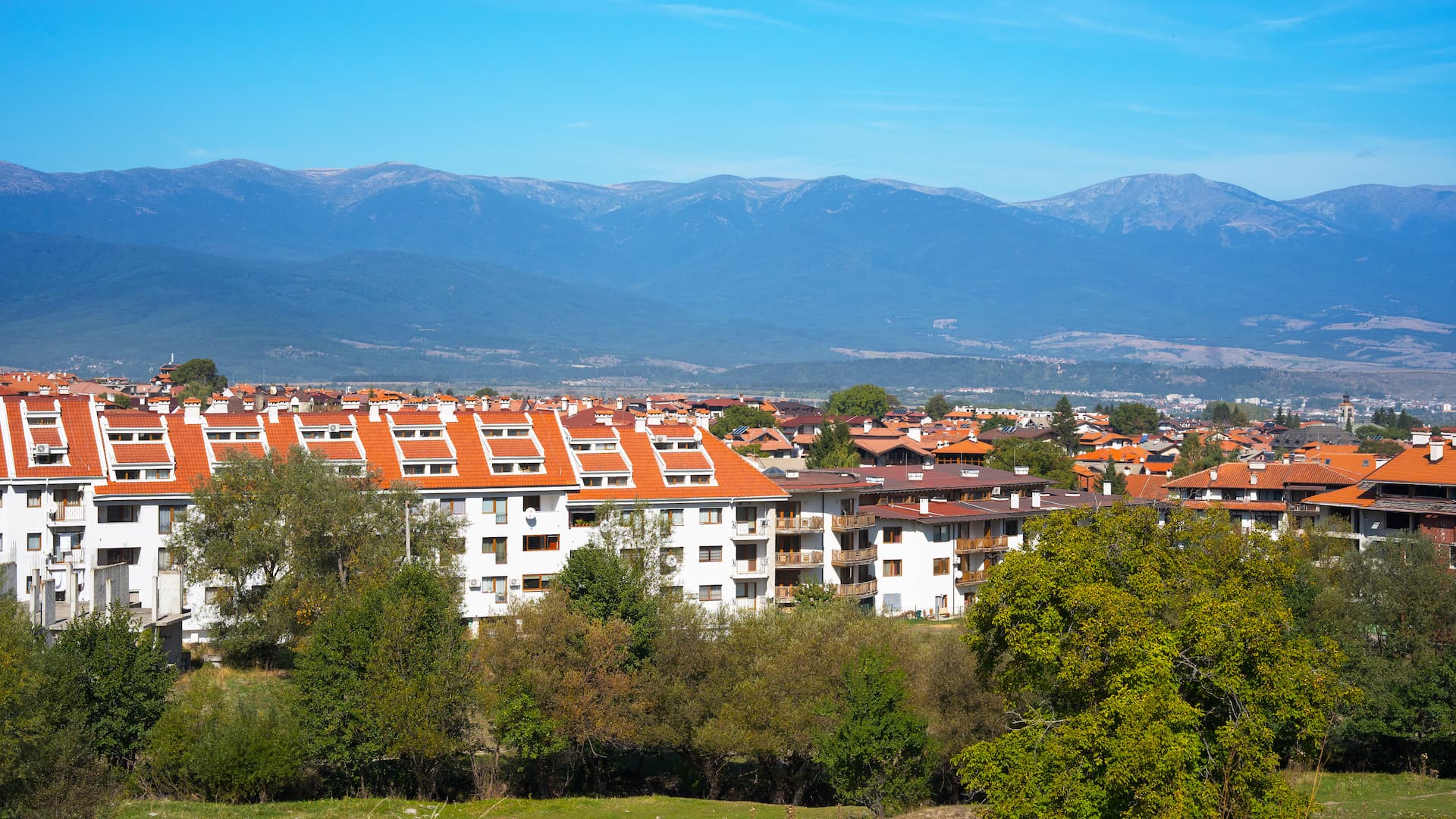 White buildings with orange roofs overlooking a valley with large blue mountains in Bansko.
