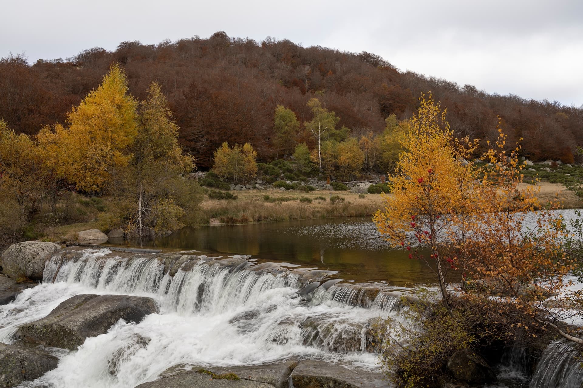 Waterfall cascading over rocks into a lake with autumn foliage in Lozère, Pont-de-Montvert.