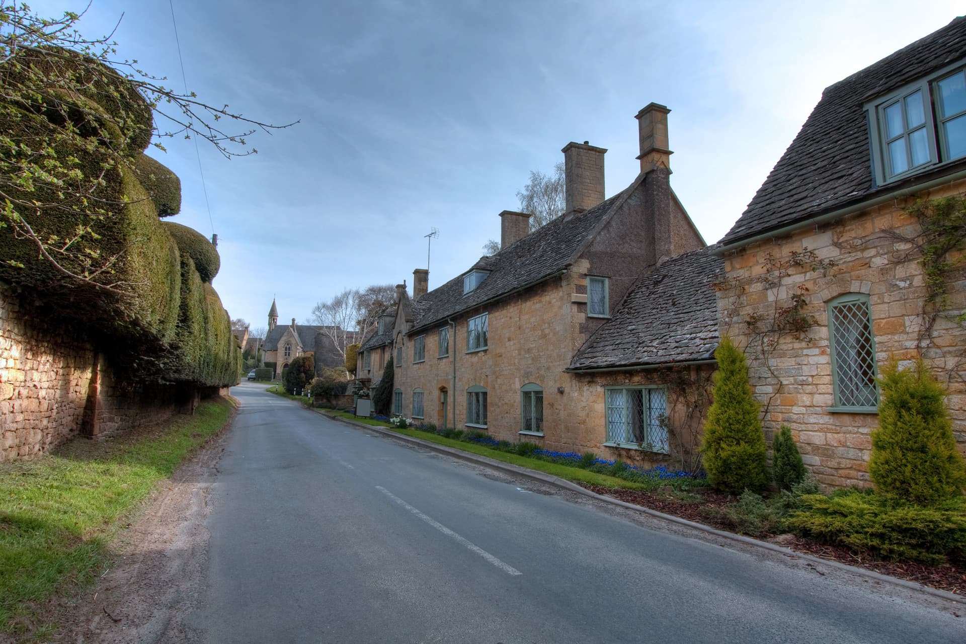 Cotswold stone cottages lining a road in Broad Campden village with a church spire visible.