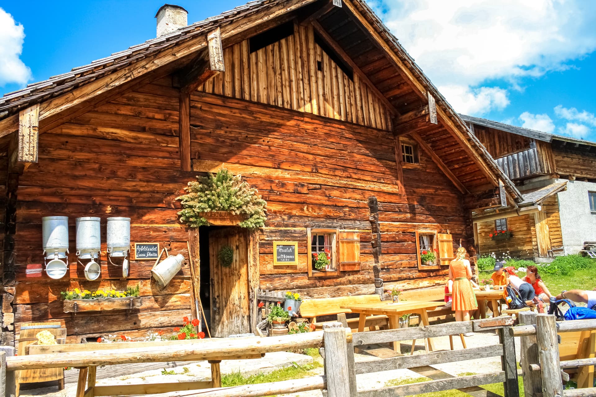 Rustic wooden alpine hut with outdoor seating under a bright blue sky.