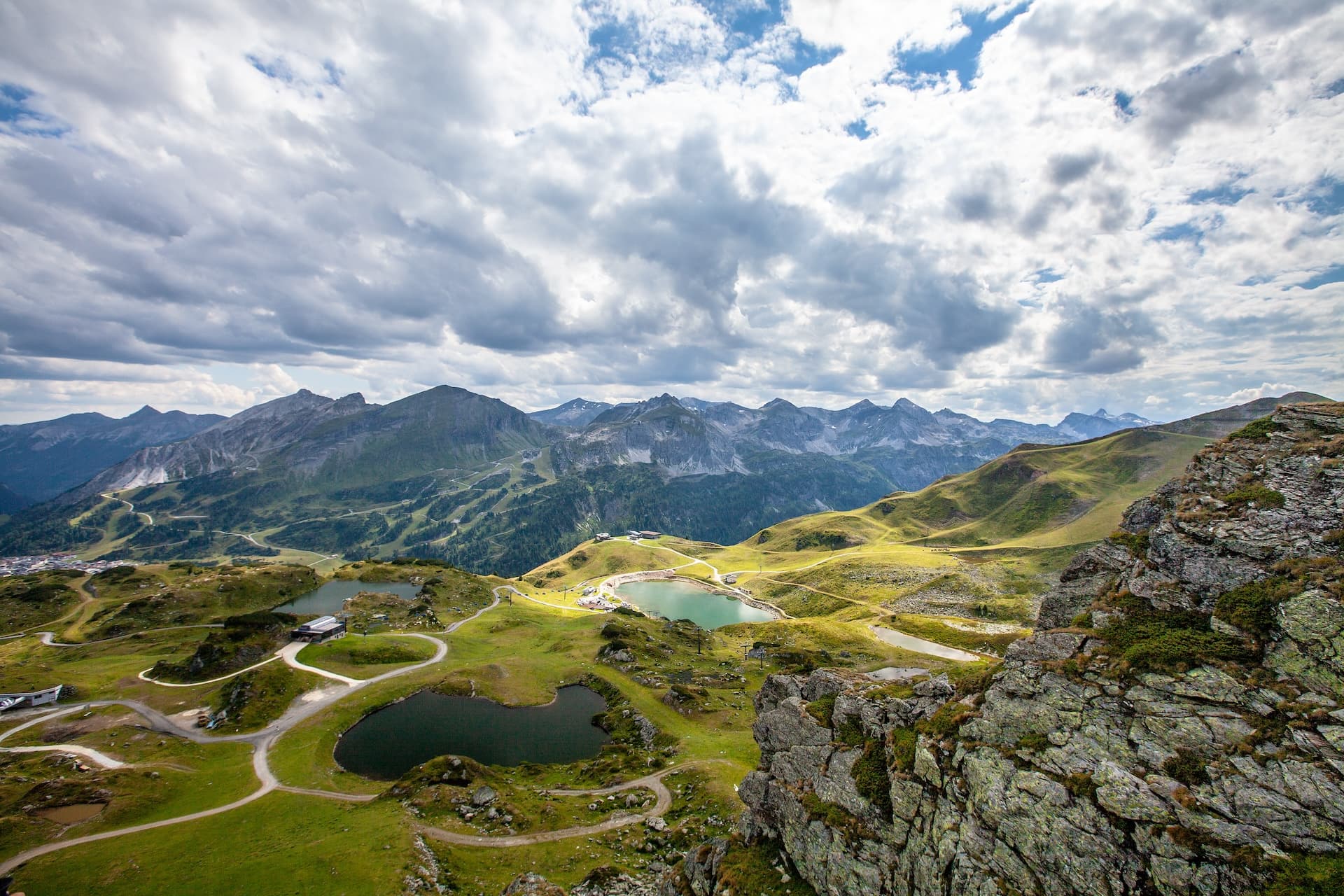 Alpine lakes and hiking trails near Krummschnabelsee, Obertauern, with dramatic mountain range under cloudy sky.