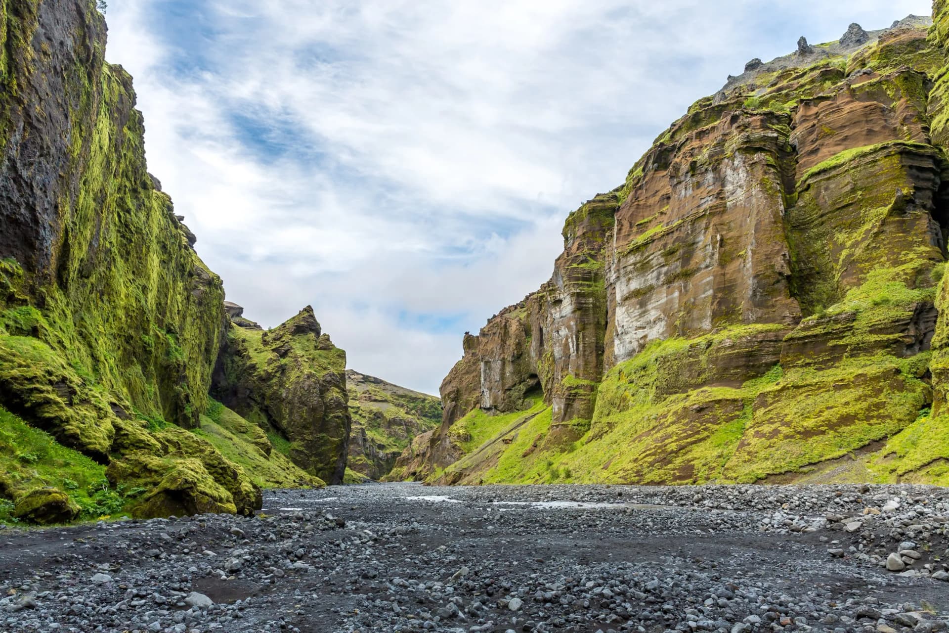 Hiking path through a canyon with steep, moss-covered cliffs and a rocky riverbed.