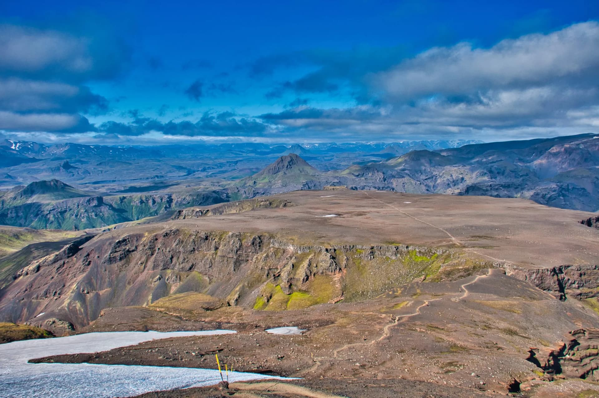Hiking near Fimmvörðuháls pass across rugged volcanic landscape with snow patches and blue sky.