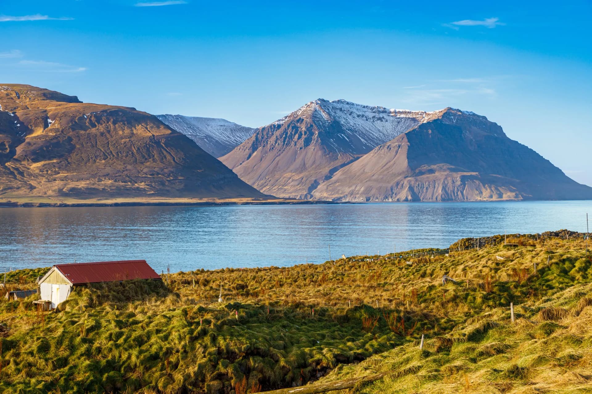 Borgarfjordur Eystri landscape with snow-capped mountains, water, and a small white building with a red roof.