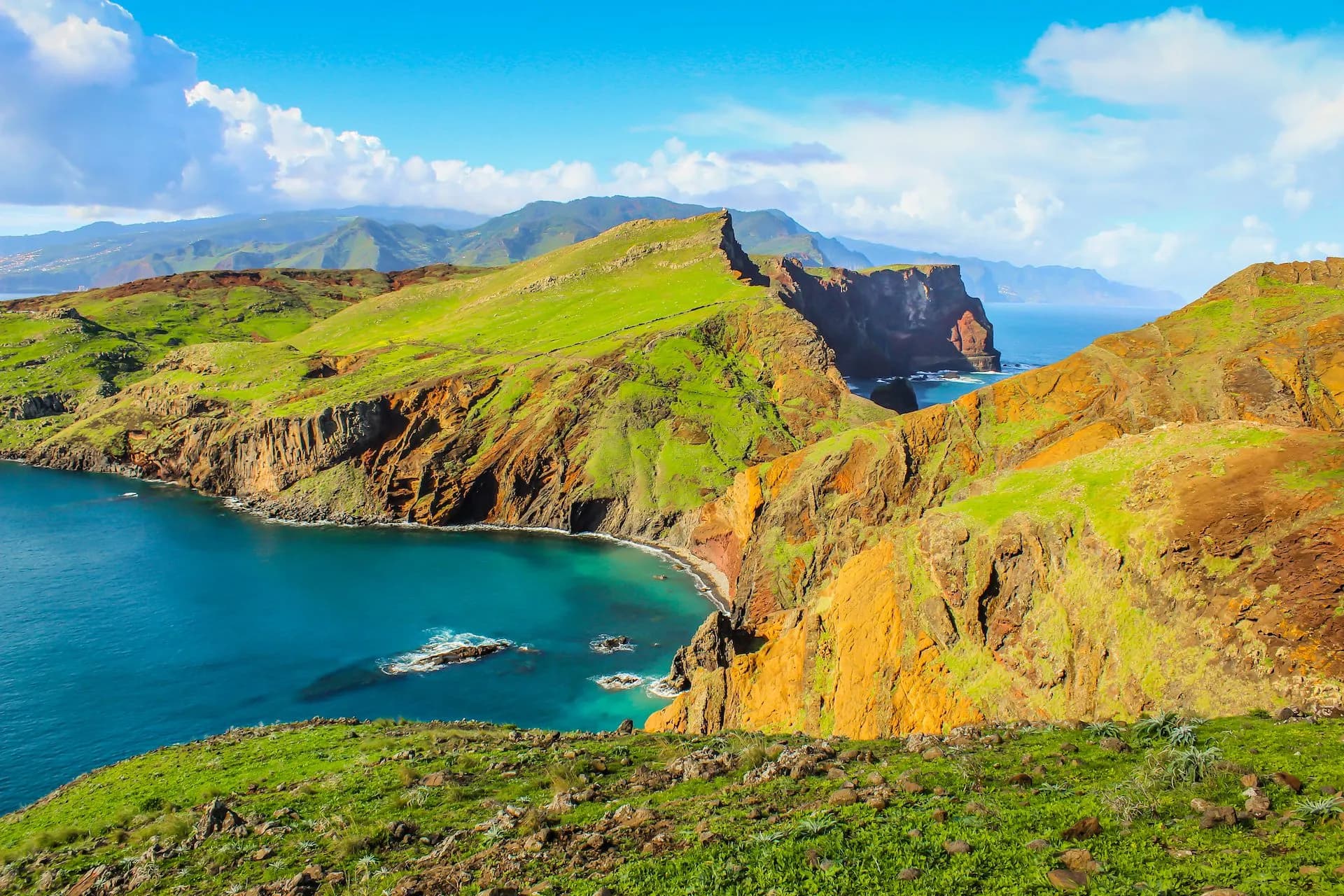 Ponta de São Lourenço dramatic green and orange cliffs meeting turquoise ocean under a blue sky.