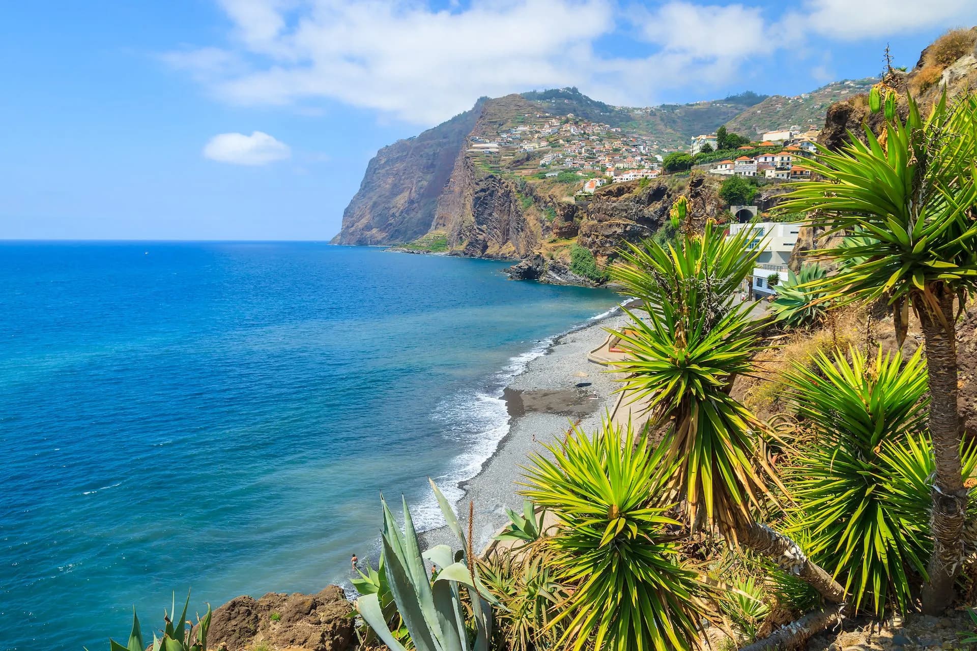 Coastal view of Cabo Girao with steep cliffs, town on hillside, and blue ocean water.