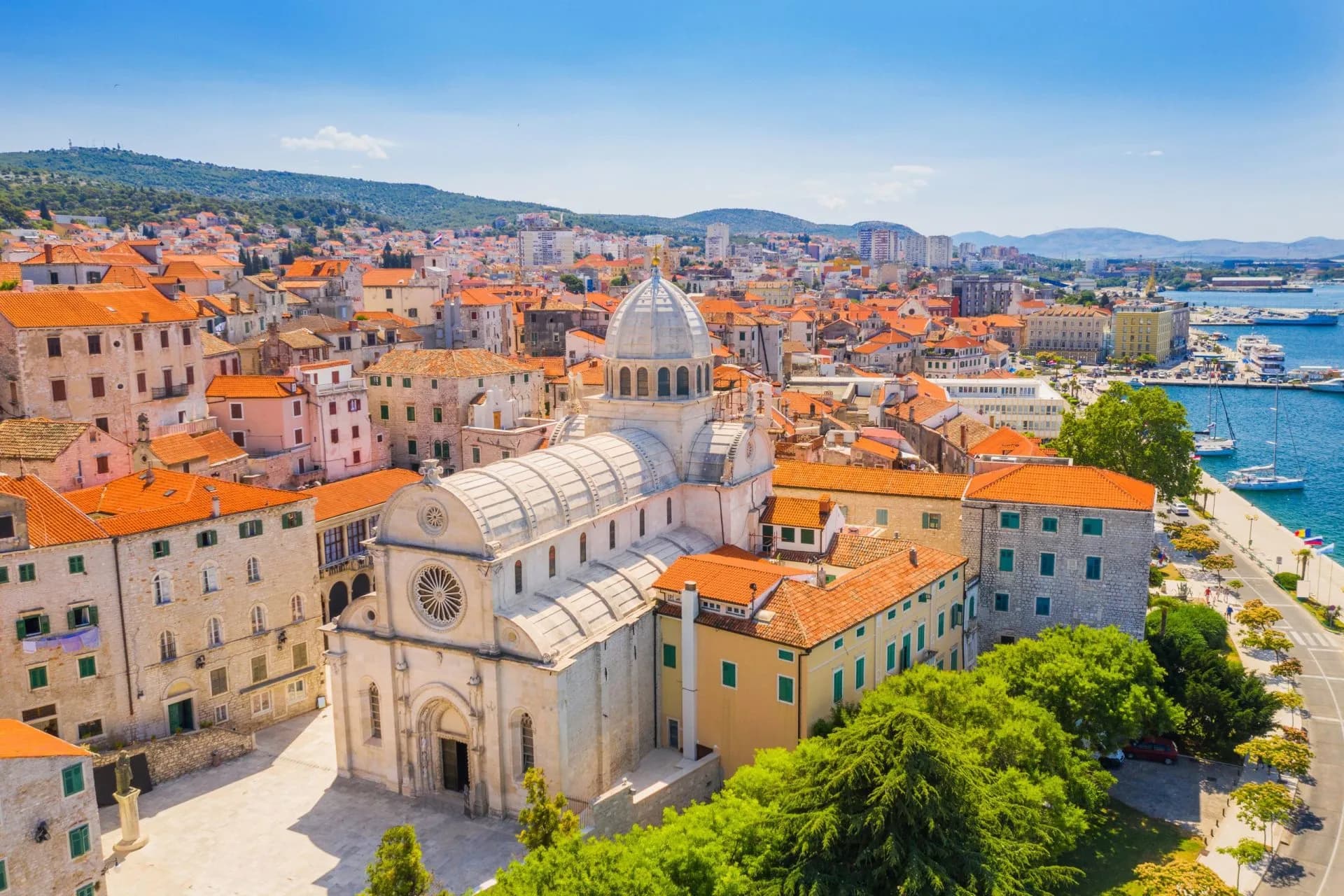 Old town of Šibenik with St. James Cathedral, terracotta roofs, and harbor on a sunny day.