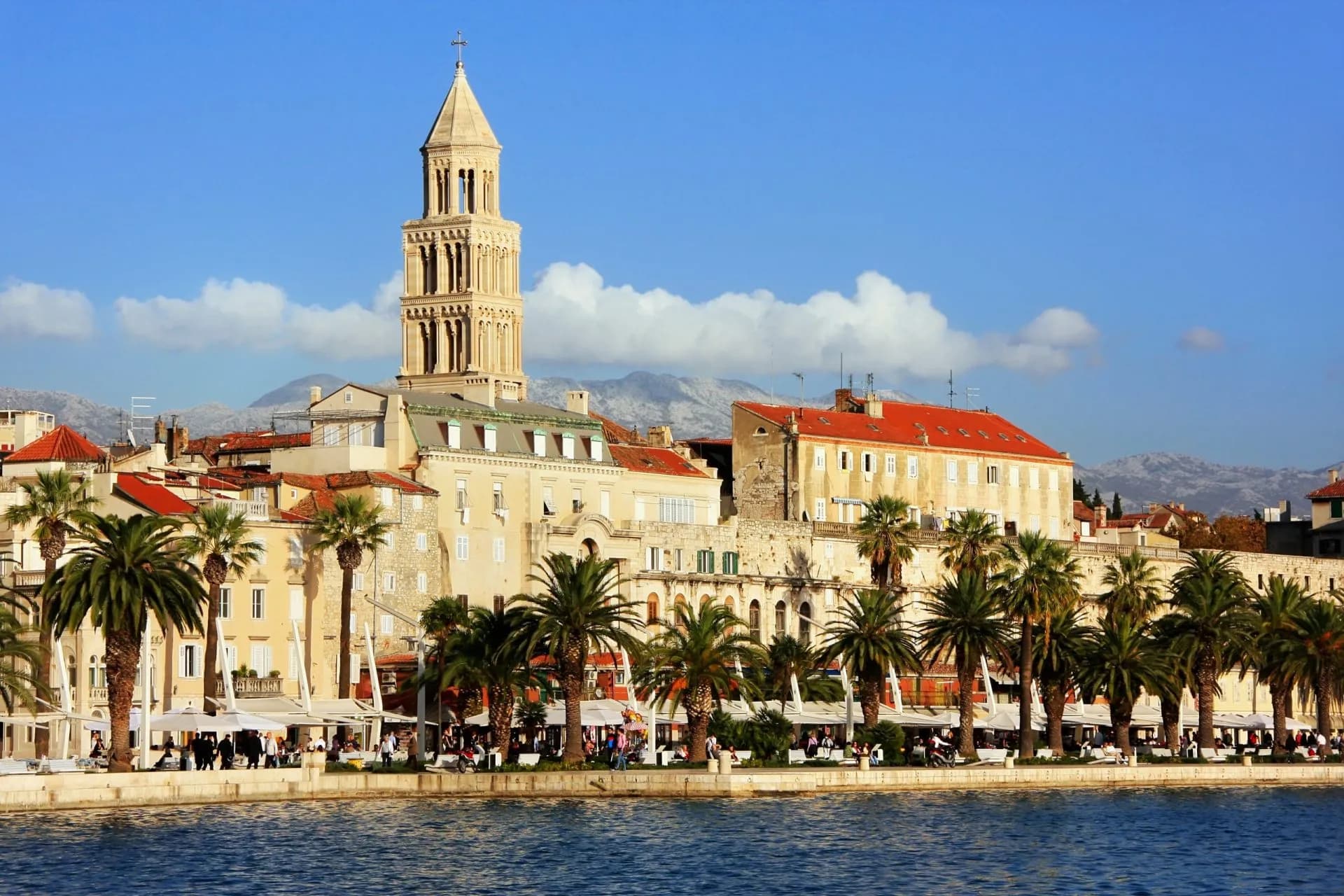 Bell tower and palm trees along waterfront promenade with mountains in Split, Croatia