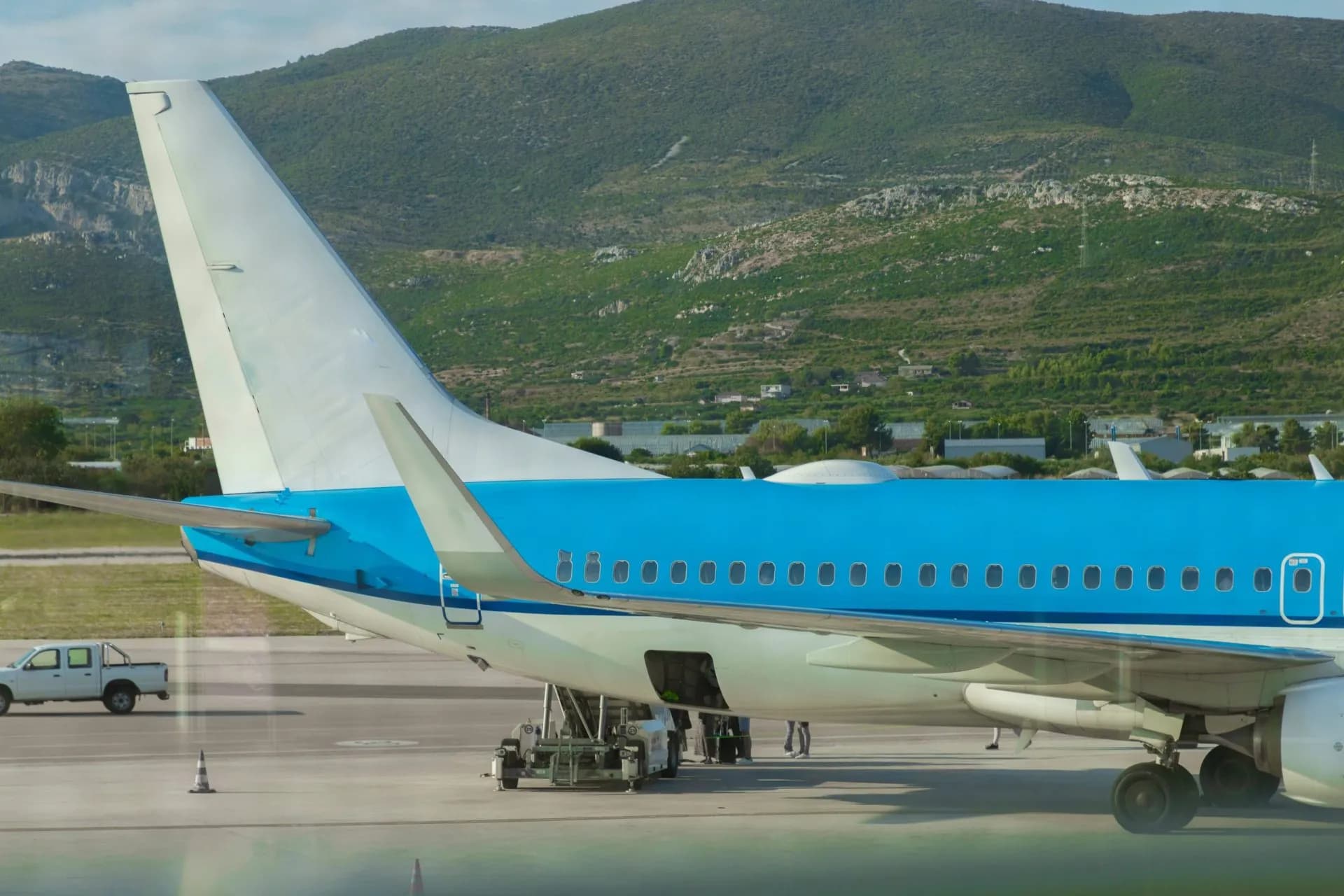 Airplane tail and wing on tarmac with green, scrub-covered mountains in the background