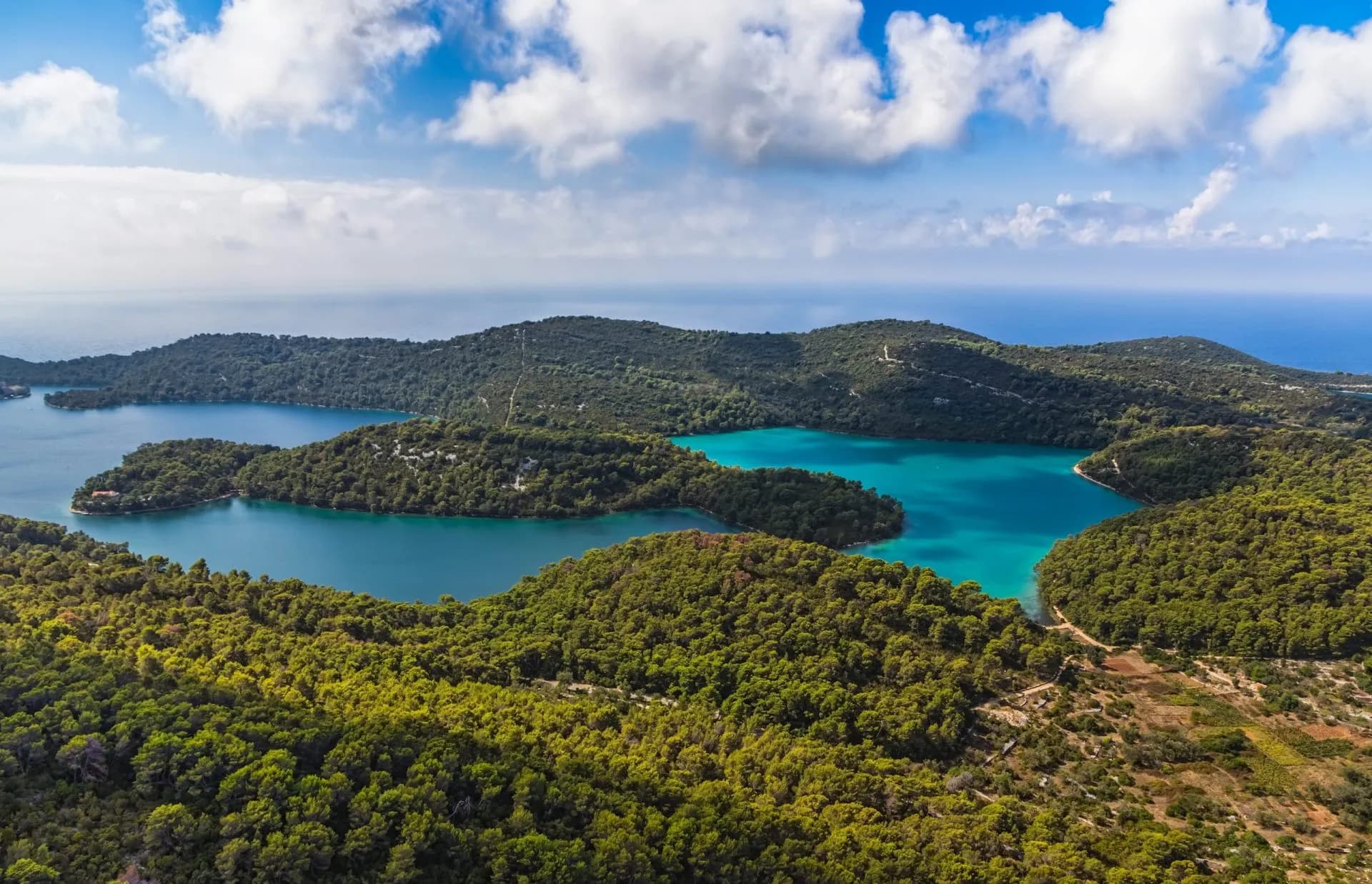 Aerial view of lush green hills surrounding turquoise lakes connecting to the open sea, Mljet, Croatia