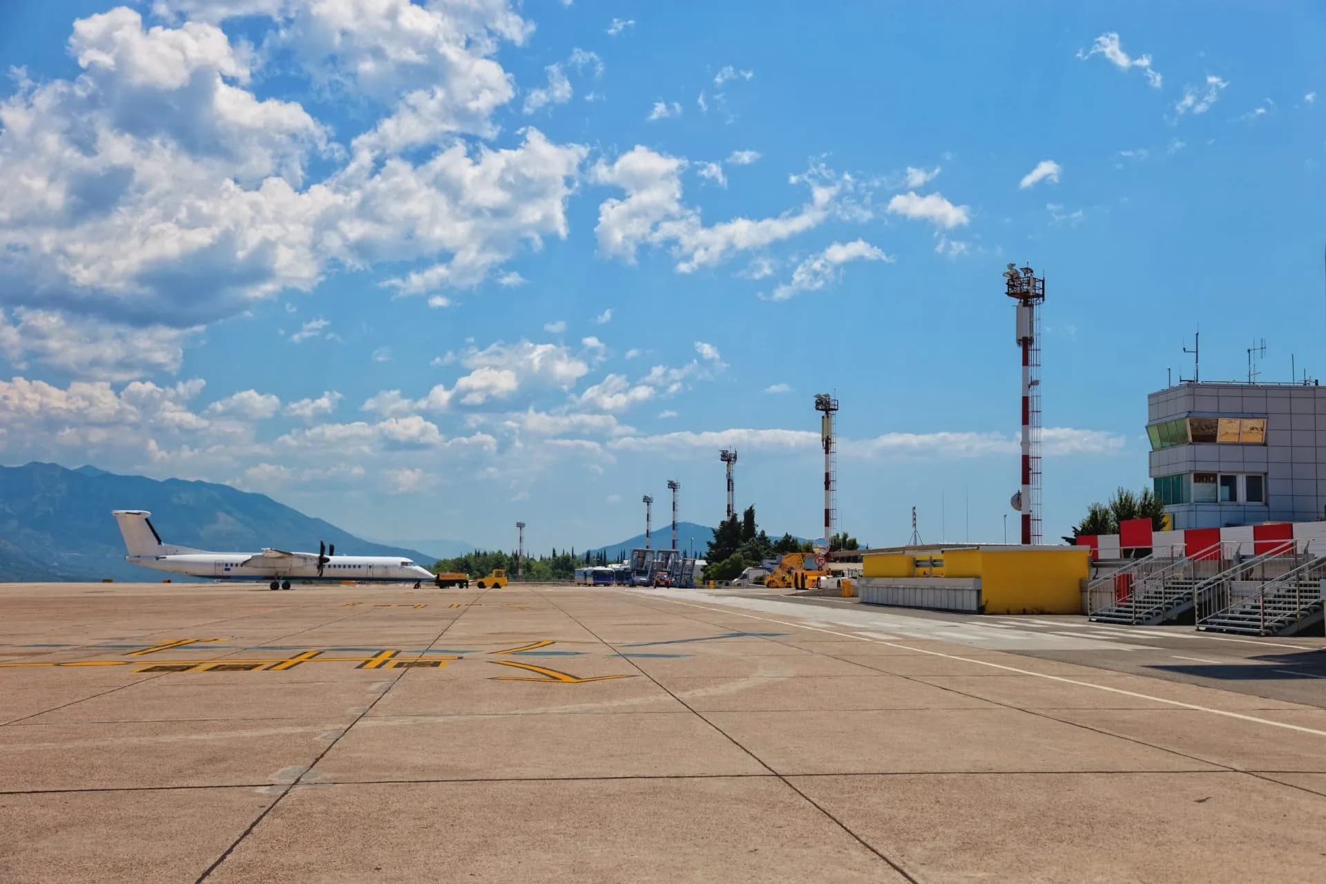 Turboprop airplane on tarmac at Dubrovnik Airport with control tower and mountains in background.