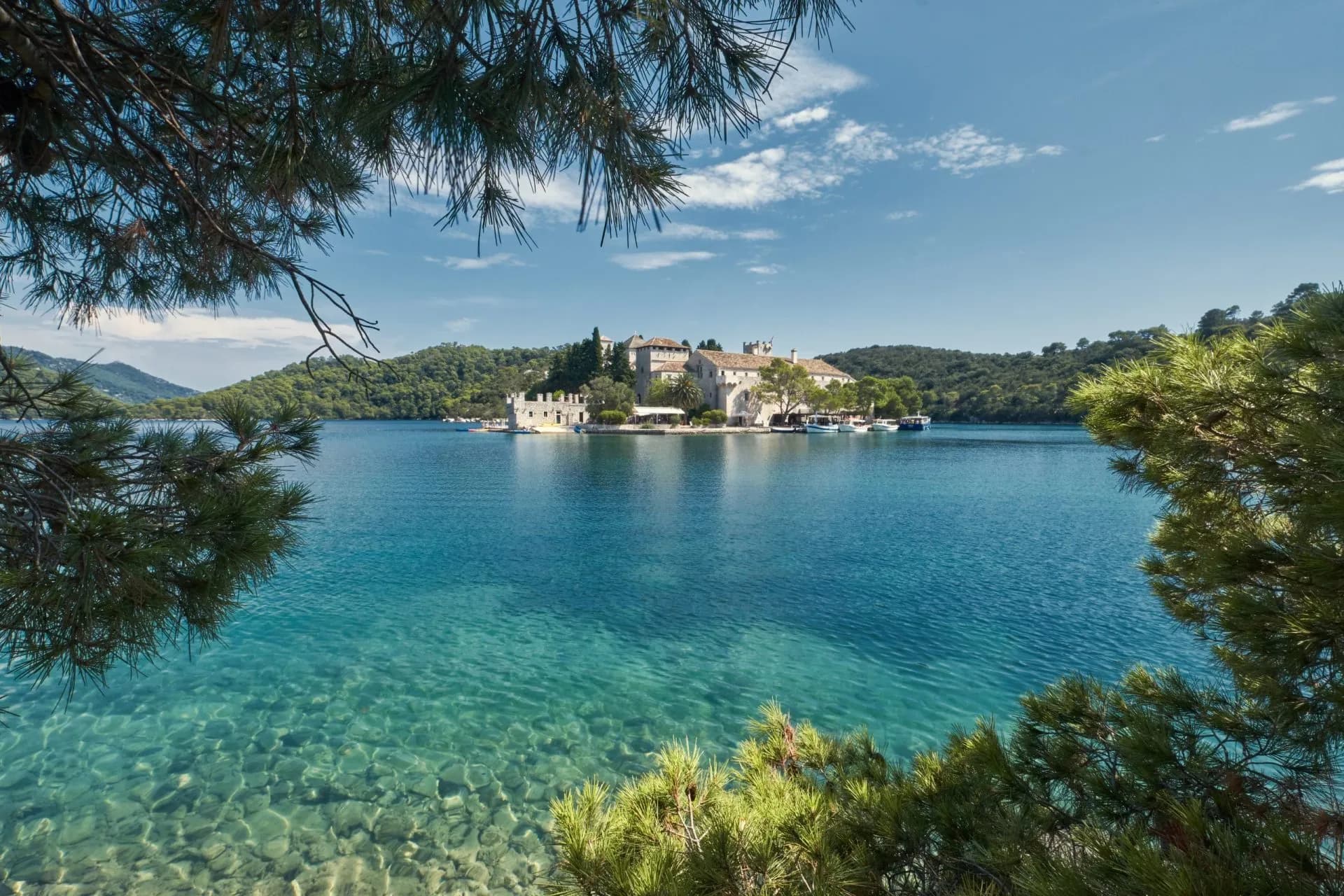 Saltwater lake with clear turquoise water and a monastery island framed by pine branches, Mljet.