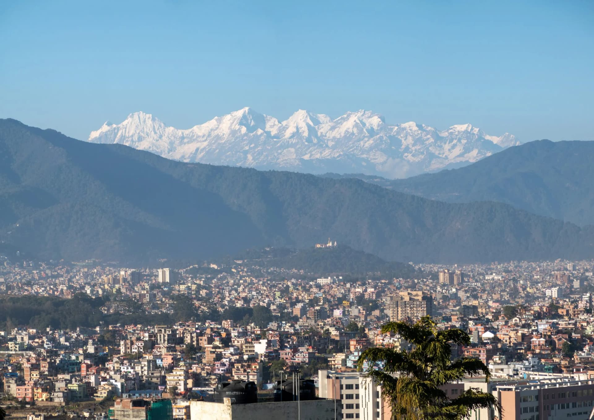 City of Kathmandu sprawling below hazy green hills and snow-capped Himalayan peaks.
